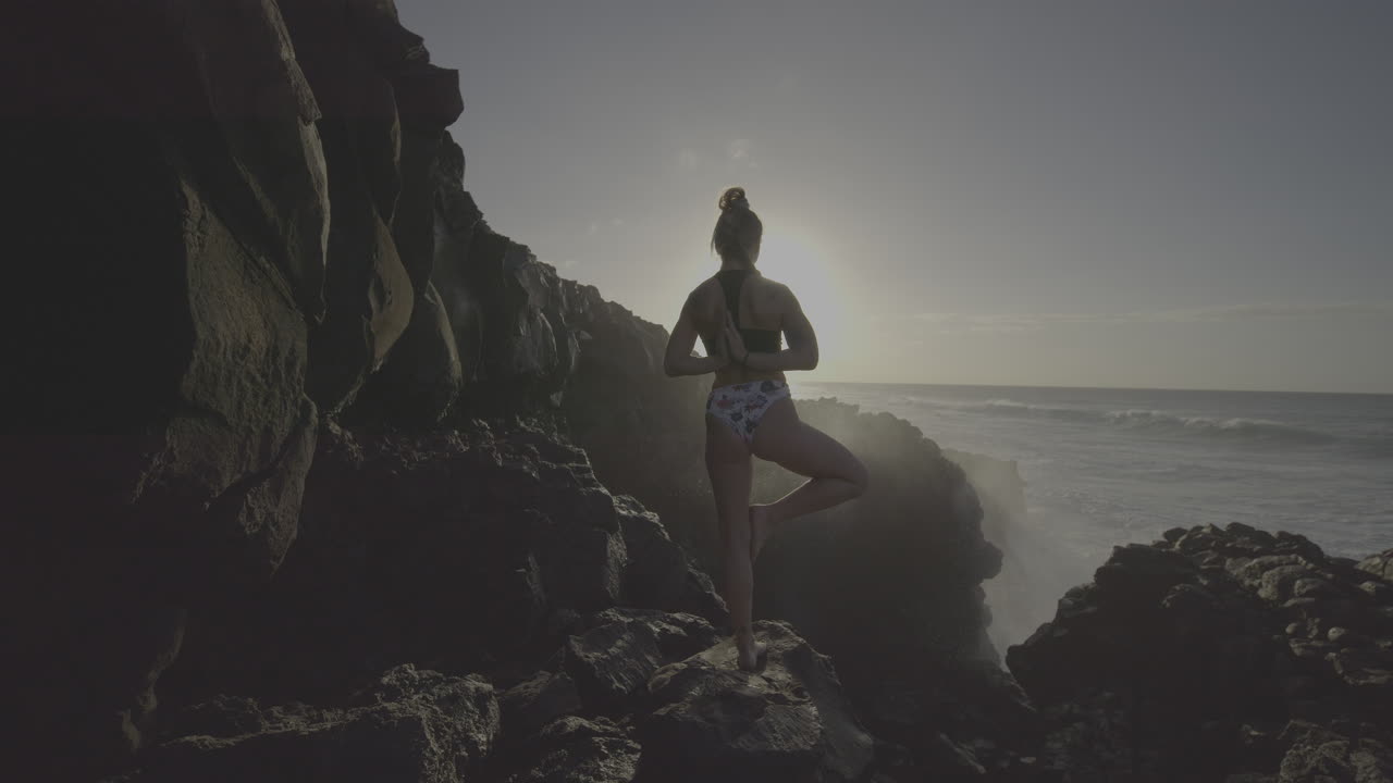 Woman in Yoga Pose on a Rocky Beach at Sunrise