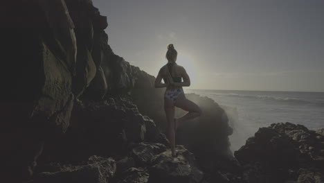 woman in yoga pose on a rocky beach at sunrise