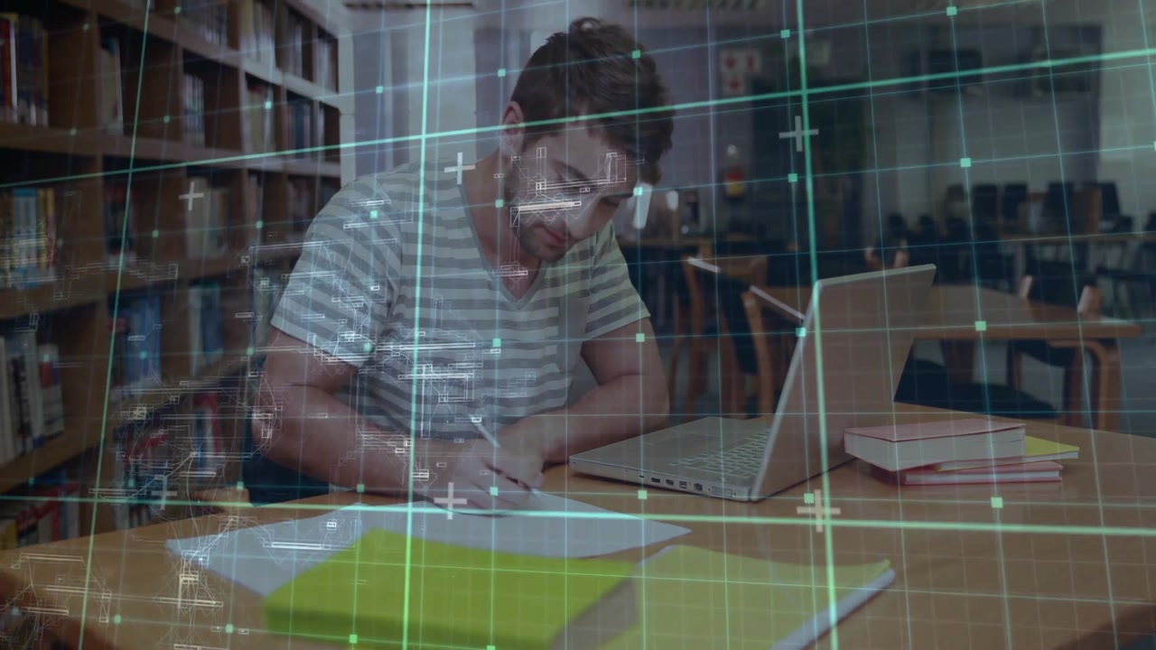 Male student picking up pen, writing academic notes and typing on laptop under grid overlay