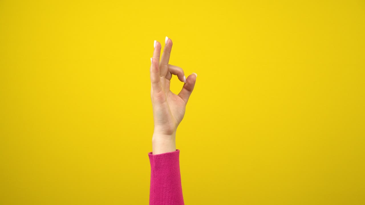 женская рука показывает знак ok. студийная фотография на изолированном желтом фоне.