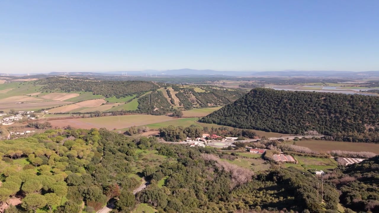 Veja de la Frontera, Província de Cádis, Espanha. Filmagem panorâmica de drone da vista e da paisagem rural que cerca o famoso Pueblo Blanco, empoleirado no topo de colinas arborizadas sob sol forte com céu azul claro