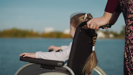 blonde preschooler girl sits in wheelchair looking at river