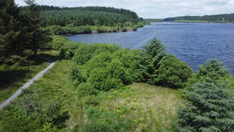 idyllic blue water reservoir lake woodland hiking walk aerial view low dolly right over trees