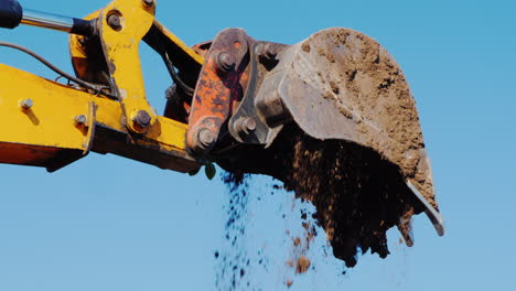 from the excavator bucket pouring soil against the blue sky