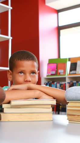 niños de la escuela apoyados en una pila de libros en la biblioteca