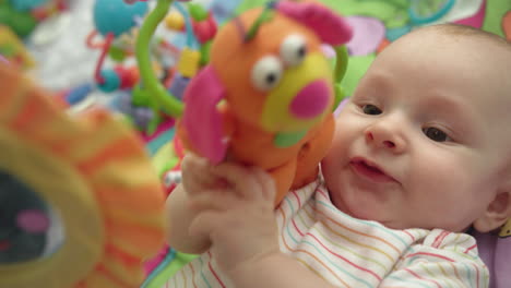 Sweet-baby-playing-toy.-Close-up-of-cute-baby-boy-lying-on-colorful-mat