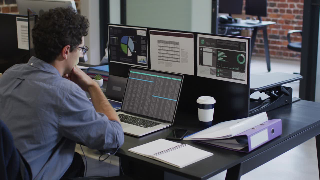 hombre caucásico sentado en el escritorio codificando datos en una computadora portátil