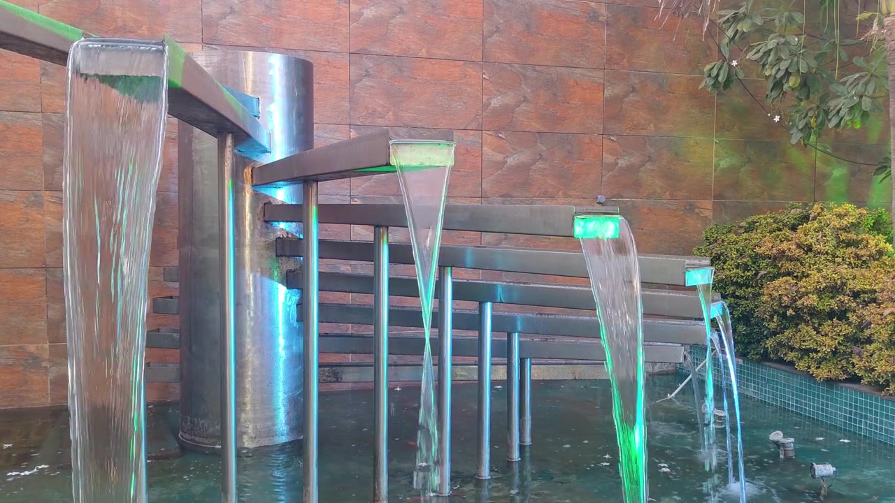 Fuente moderna con múltiples chorros de agua que fluyen de elegantes estructuras metálicas, iluminada por luces vibrantes.