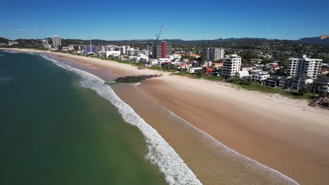 aerial view of rocky groyne in the middle of the sandy seashore at palm beach coastal suburb in qld, australia