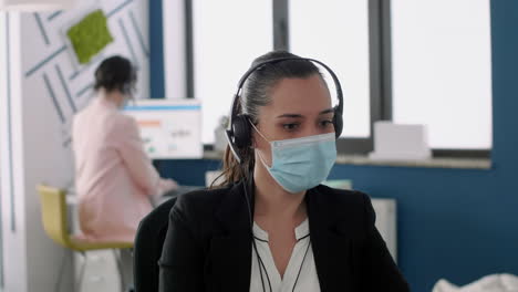 close up of executive manager with face mask and headset working on laptop computer