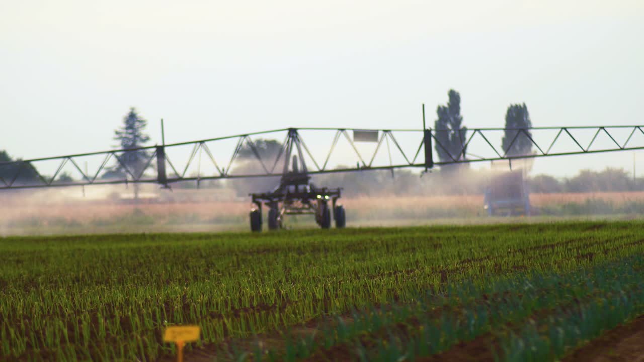 Agricultural wide arm pesticide sprayer, automatically slow moving through a field of multiple crop trials on a windy day, selective focus