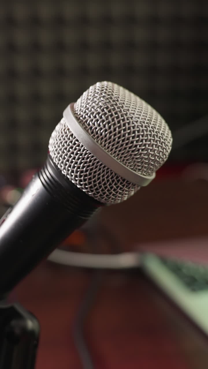 fotografía de primer plano de un micrófono en un soporte con un fondo borroso con un altavoz, auriculares y una computadora. la escena captura los elementos esenciales de un estudio de grabación