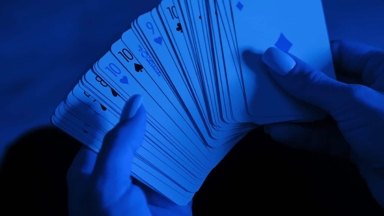 Artistic close up of woman fanning play cards under strong blue lighting indoors