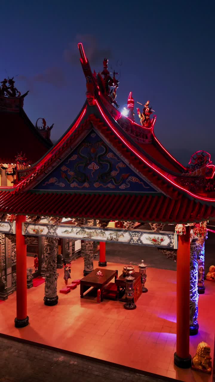 This vertical video shows the entrance of a Buddhist temple featuring intricate carvings and a single person engaged in prayer offering a glimpse into the calm spiritual atmosphere