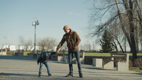 a father holds his son's hand while keeping his other hand in his jacket pocket, the young boy moves playfully, casting shadows on the pavement