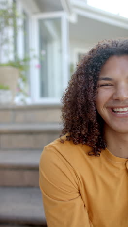 vertical video half portrait of happy biracial man with long hair in sunny garden, slow motion