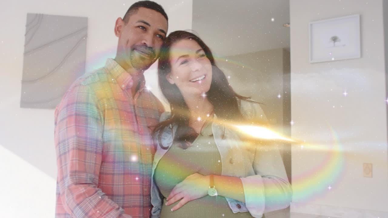 Man placing hands on pregnant woman's belly, camera pulling back, sparkles showing maternity joy