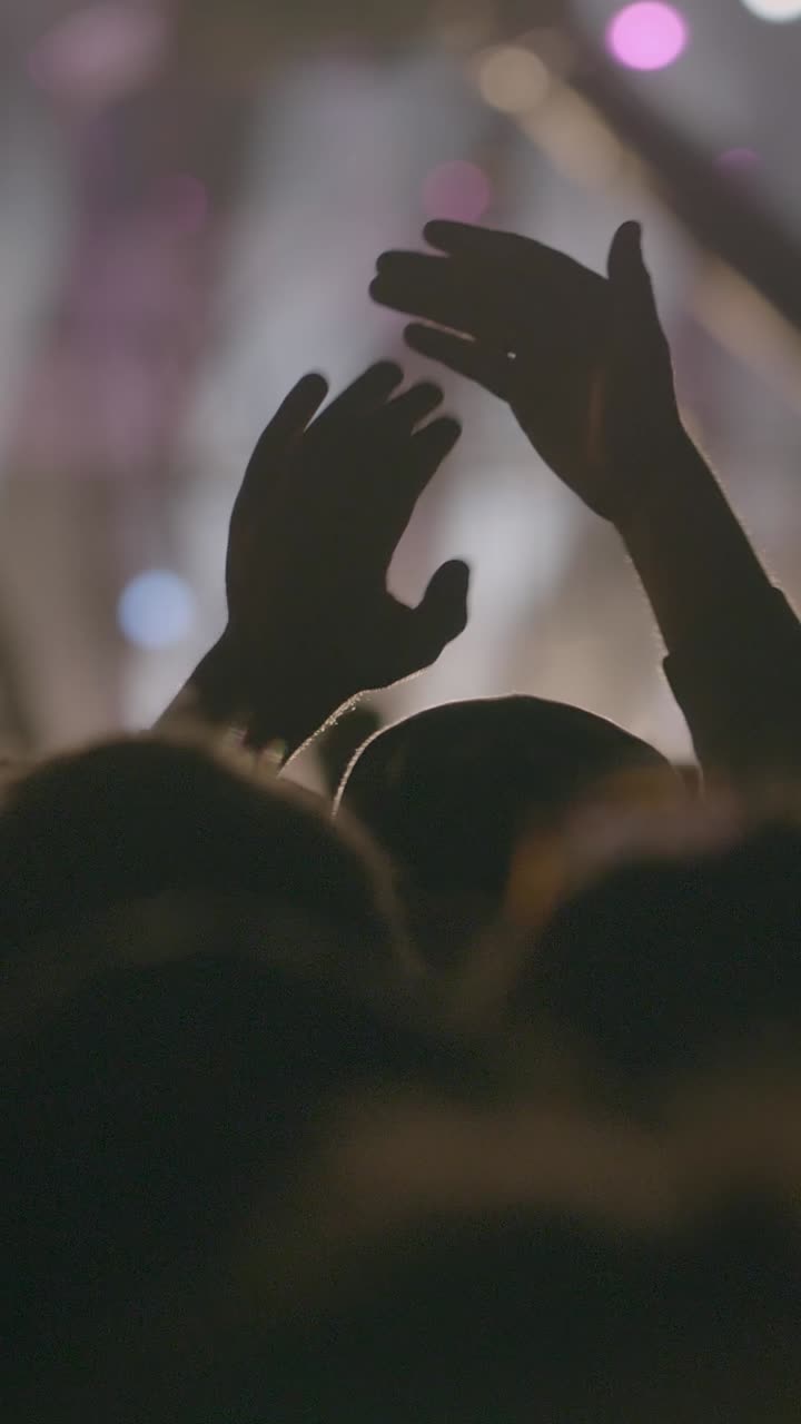 Mani in silhouette che applaudono e acclamano a un concerto dal vivo