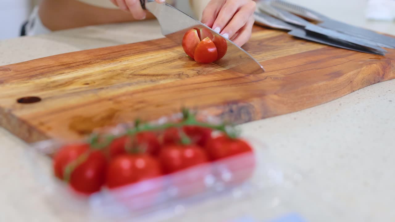 A person slices tomatoes on a wooden cutting board in a bright kitchen setting