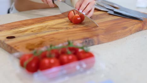 a person slices tomatoes on a wooden cutting board in a bright kitchen setting