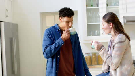 happy diverse couple talking and drinking coffee in kitchen at home, in slow motion