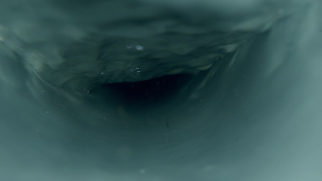Vista interior de um tubo de drenagem escuro com fluxo de água agitado. Perspectiva em close-up mostrando correntes líquidas turbulentas e textura úmida usando uma lente sonda.