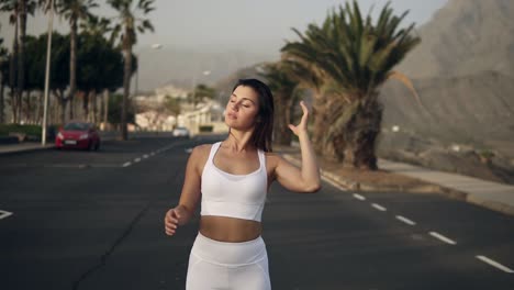 joven mujer bronceada con ropa blanca posando de pie en la carretera