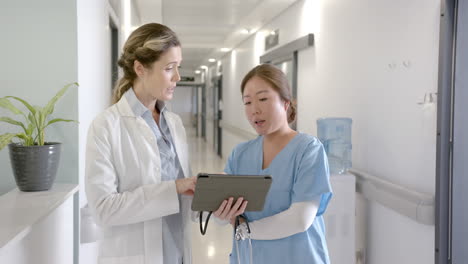 portrait of happy diverse female doctors using tablet talking at hospital reception, slow motion