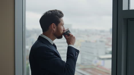 side view thoughtful businessman drinking coffee at office window close up.