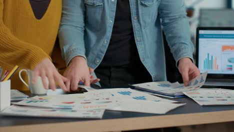 selective focus on coworkers hands going through business papers with sales charts and key profit indicators