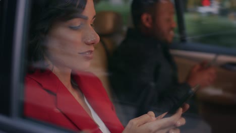 una joven y un hombre viajan en el asiento trasero de un coche por la noche. ambos usan teléfonos inteligentes, navegan por internet y hacen trabajo de negocios. la toma de la cámara fue hecha desde fuera del coche.