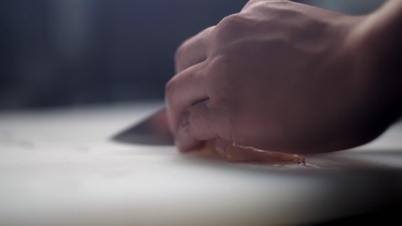 Slow motion close up view of a Chef hands slicing squid tubs with a knife