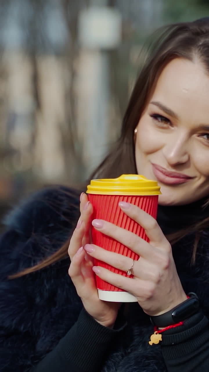 Fashion outdoor video of beautiful sensual girl with dark hair wearing luxurious fur coat,holding paper cup with coffee. Vertical video