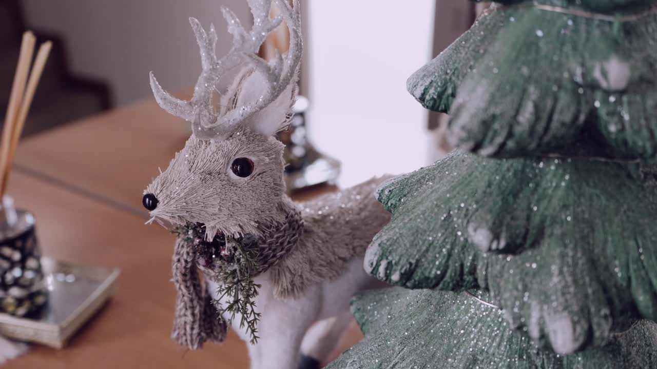 Decorative reindeer figurine with scarf beside a glittery christmas tree indoors