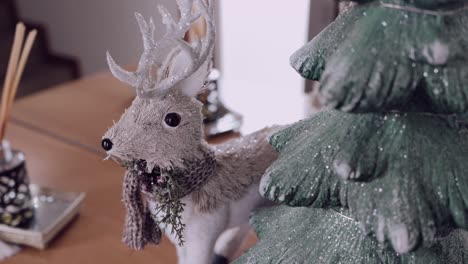 Decorative reindeer figurine with scarf beside a glittery christmas tree indoors