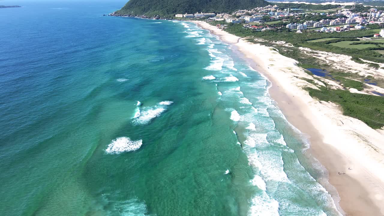 escena aérea de drones de playa paradisíaca con océano azul turquesa y verde esmeralda con montañas y complejo vacacional para turistas frente a la playa en verano en florianópolis playa santinho