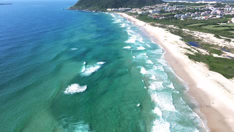 aerial drone scene of paradisiacal beach with turquoise blue and emerald green ocean with mountains and vacation resort for tourists facing the beach in summer in florianópolis santinho beach