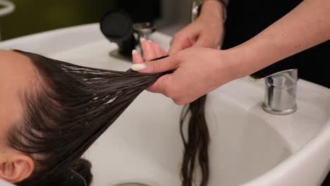 rinsing long wet hair in beauty salon sink. close up of long wet hair being rinsed with water in a professional beauty salon during a hair washing treatment