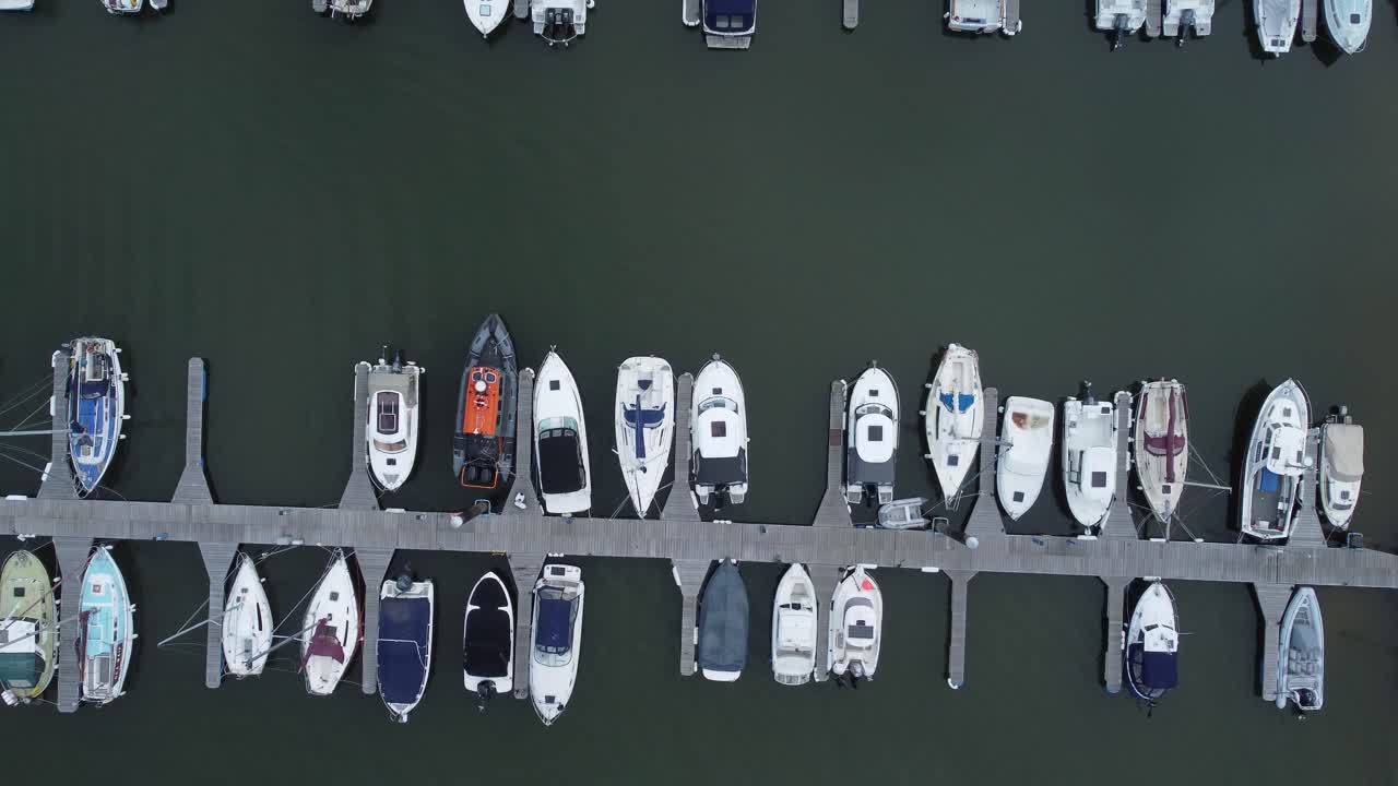 Top down aerial drone view above luxury moored private marina sailing ships and yacht boats slow forward shot