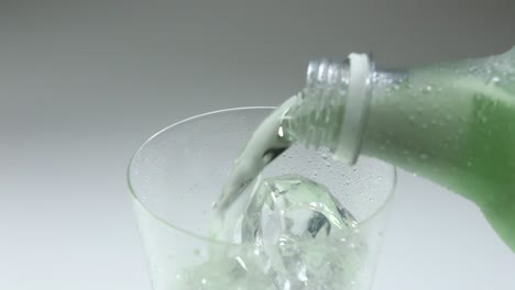 glass with ice into which a greenish drink from a plastic bottle is poured