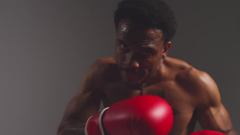 Close-Up-Studio-POV-Shot-Of-Tattooed-Male-Boxer-Throwing-Punch-Towards-Camera-With-Gloves-In-Boxing-Match-Against-Grey-Background