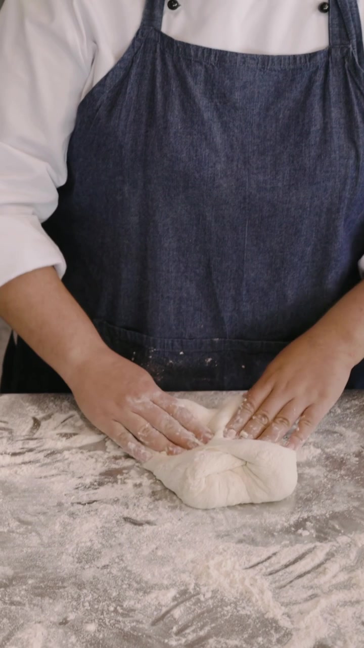 Video vertical: Estirando masa, panadero con delantal doblando, pellizcando, formando bolas sobre una mesa enharinada