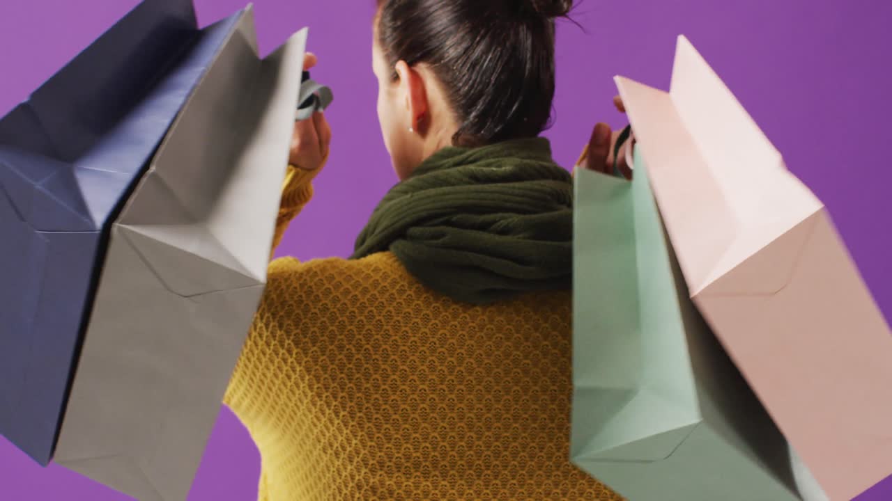 vista trasera de una mujer sosteniendo bolsas de regalos de colores sobre fondo púrpura