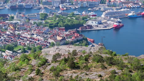 Drone-shot-from-Stoltzeleiven-and-Sandviksfjellet-with-people-enjoying-the-beautiful-view-of-the-city-centre-and-harbor-in-Bergen,-Norway-on-a-beautiful-day