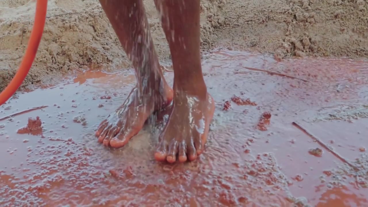 Close up of a native artisan washing their dirty bare feet with a water hose after kneading clay for pottery, an ancestral manual process