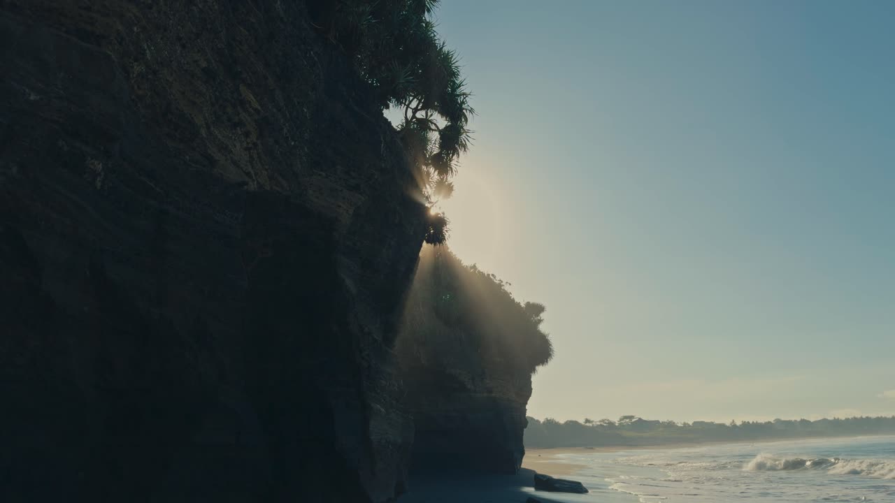 Un bellissimo bagliore solare emerge da dietro una scogliera costiera calcarea mentre la spuma dell'oceano si solleva, creando una nebbia magica.