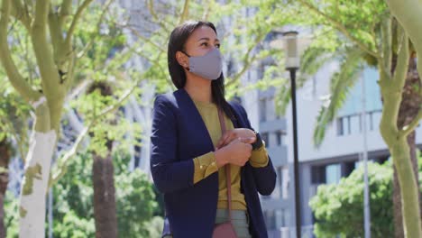 African-american-woman-wearing-face-mask-disinfecting-hands-in-the-street