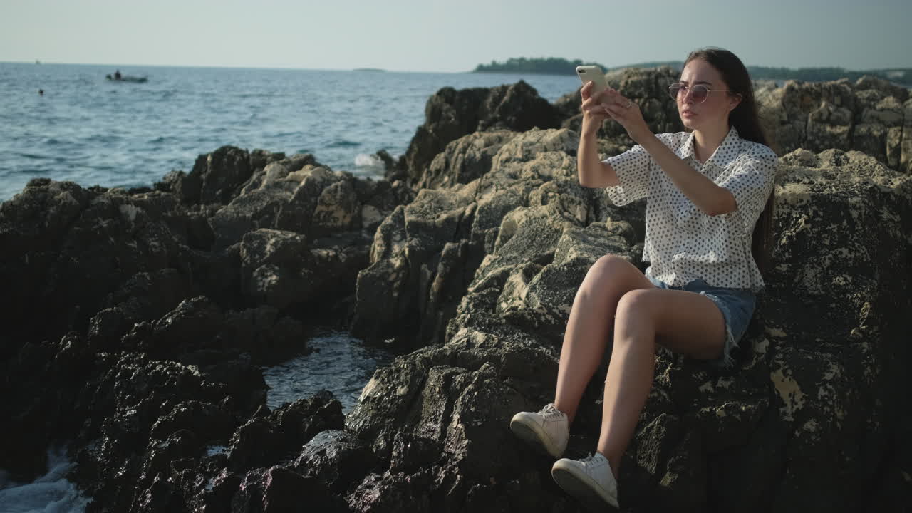 chica tomando fotos en las rocas junto al mar