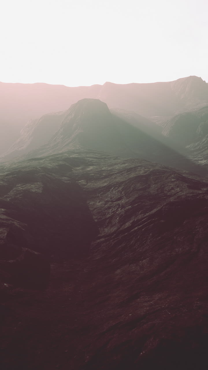 una majestuosa cordillera se levanta en la distancia, proyectando una larga sombra sobre la tierra de abajo. el cielo es de un rosa suave y desvanecido, y las nubes están teñidas de oro.