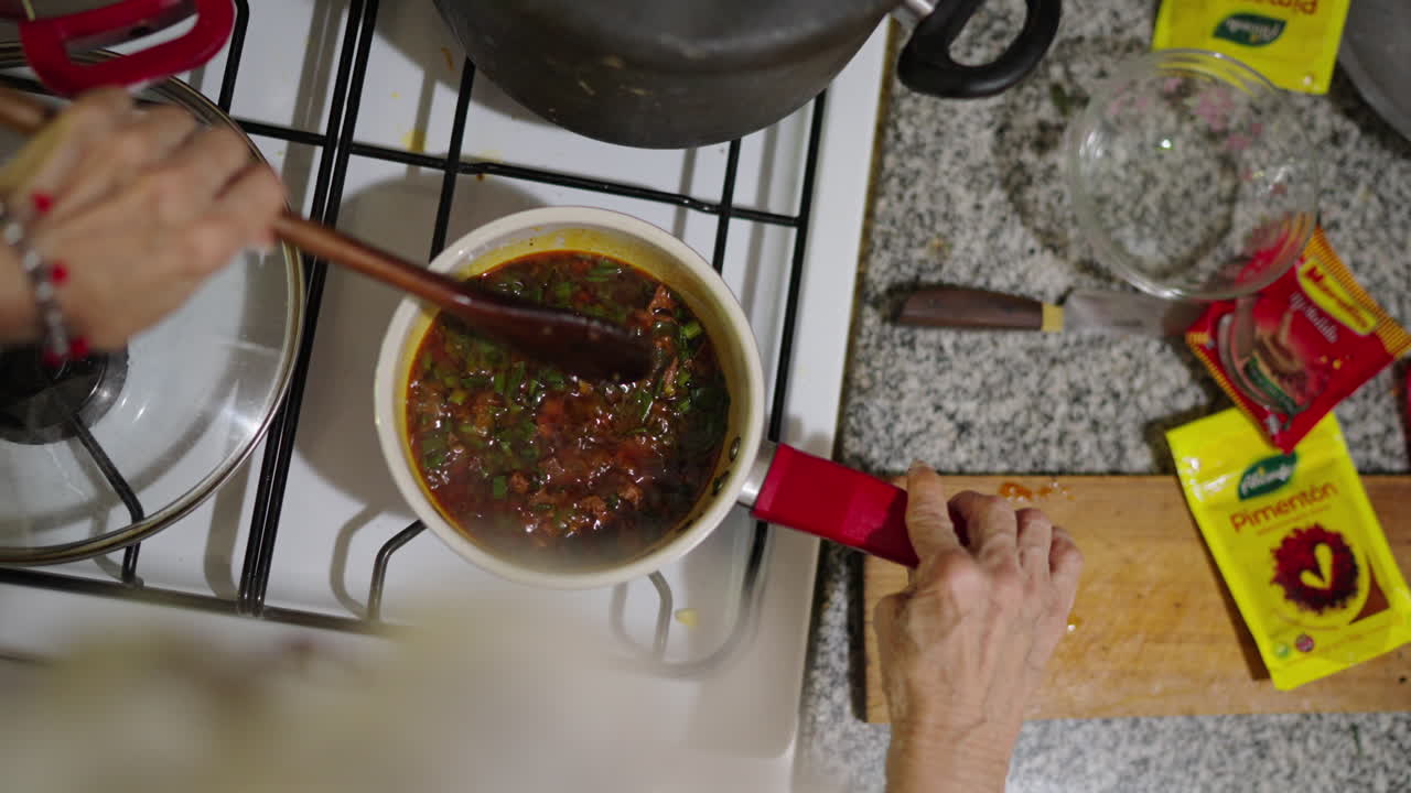 Woman's hand stirring boiling fried sauce in saucepan for Locro. Traditional argentine food, Close up